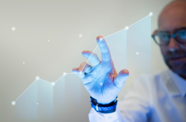 man in a white shirt and glasses pointing his finger to a growth graph